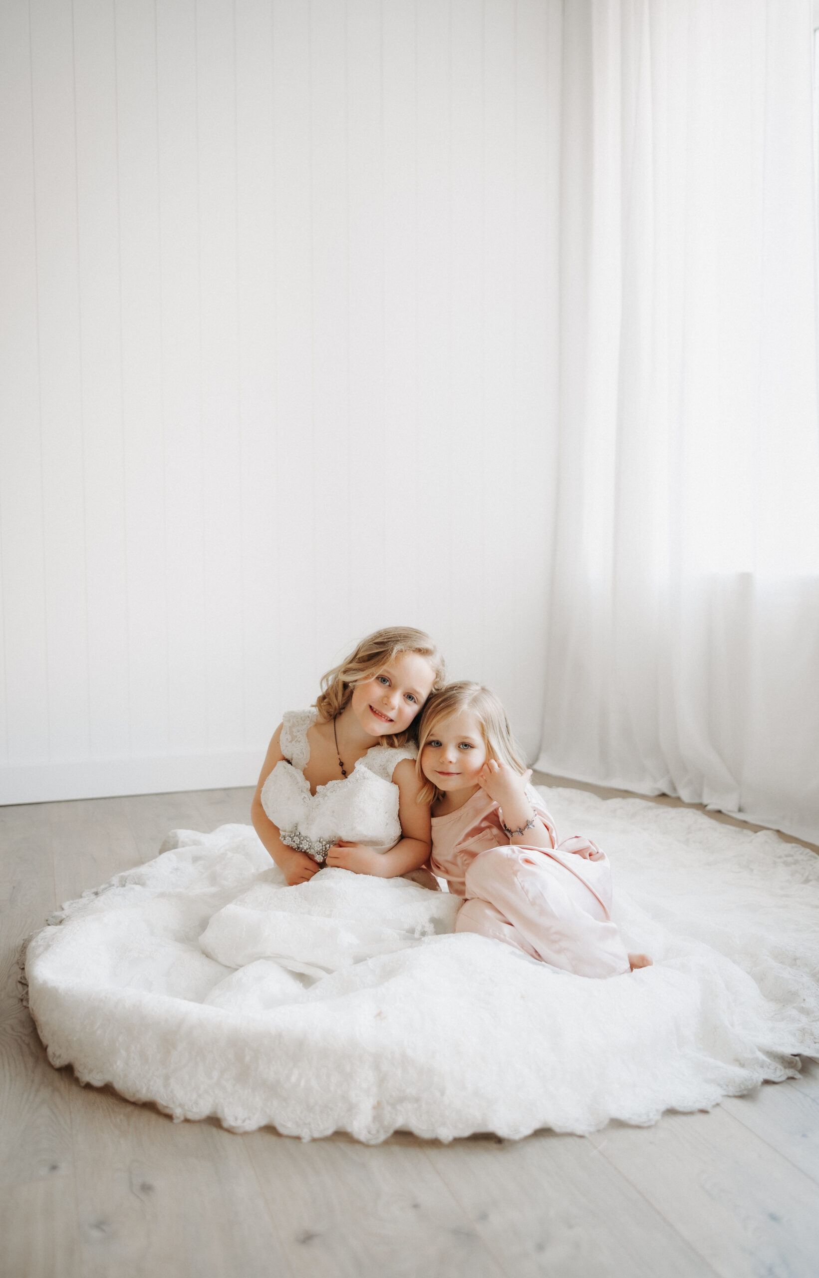 Two young girls trying on their mom’s wedding dress and smiling in the mirror during a sentimental heirloom photography session